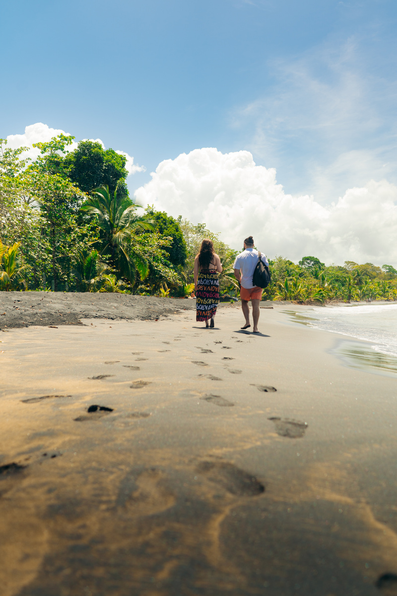 Two people walk on the sand of the  Caribbean Sea, leaving footprints in the sand