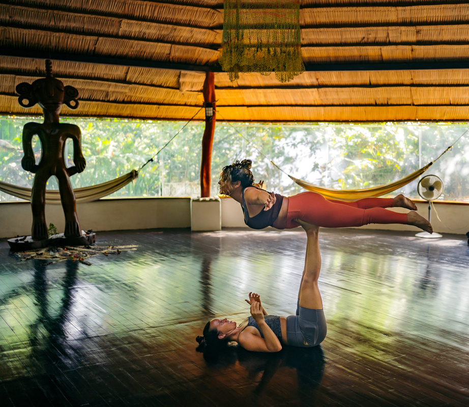 Two women practice an aerial yoga post in our open-air yoga palapa overlooking the lush green Costa Rican rainforest